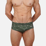 Man wearing green swim briefs with geometric pattern on a white background