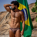 Model wearing Bikini Caio Brazilian swim brief in Astral Soil (Brown) holding Brazilian Flag
