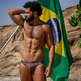 Model wearing Bikini Caio Brazilian swim brief in Astral Soil (Brown) holding Brazilian Flag
