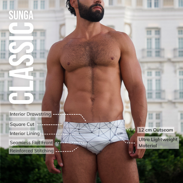 Man wearing a white swim brief with geometric pattern, standing outdoors with building in background