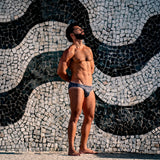 model standing against a mosaic wall with wearing caio bikini stellar ash swim brief
