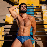 Filipe leaning against outdoor workout equipment wearing a caio slim celestial azure swim brief